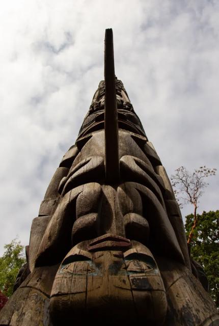 A tall totem pole featuring a large, intricately carved head at the top, showcasing vibrant colors and detailed craftsmanship